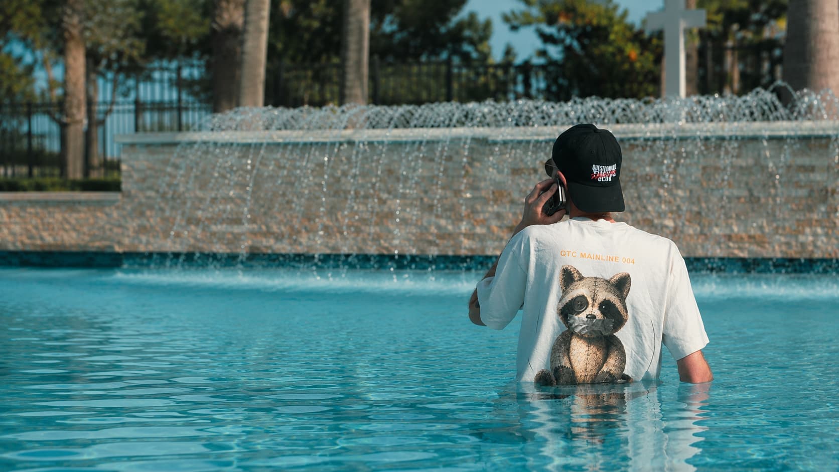 Josh wearing a QTC raccoon shirt and cap while standing in a pool